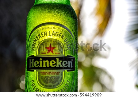 Aitutaki, Cook Islands - January 23, 2012: Close up detail of a Heineken beer bottle, illuminated by the evening sun. In the background there are palm trees on the beach of Aitutaki, Cook Islands.