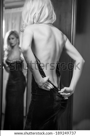 stock photo young beautiful luxurious woman zipping up her long elegant black dress looking in a large mirror 189249737