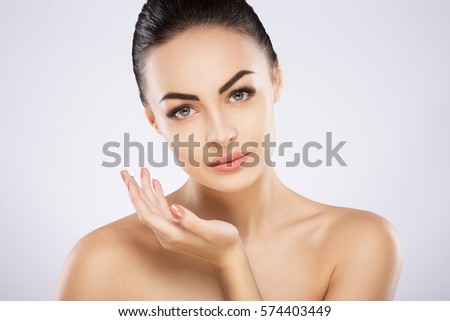 Attractive girl with black fixed hair behind, dark big eyes, soft skin and naked shoulders using cream, a model with light nude make-up, portrait, close up.