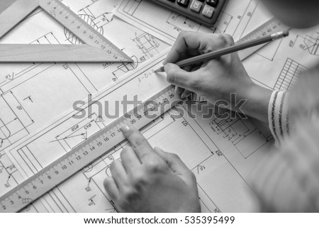 Girl architect draws a plan, graph, design, geometric shapes by pencil on large sheet of paper at office desk.