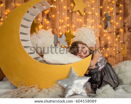 Beautiful kid girl 5-6 year old sitting smiles in a dream on a wooden month. Children's photozone. Childhood.