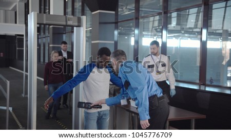 Multiracial people in airport going through gates having security control with guards.