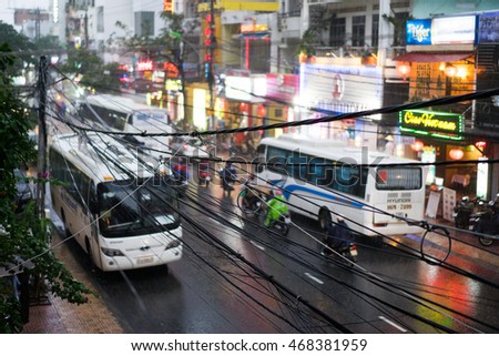 NHA TRANG, VIETNAM - JUNE 20, 2016: Evening view of the downtown with illuminated signs on the shops and busses, motorbikes and bycicles on the traffic road at rainy weather