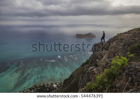 Man Standing At The Edge Of A Cliff Looking Out Over Coast Just Before Sunrise Man Standing At The Edge Of A Cliff Looking Out Over Coast Just Before Sunrise