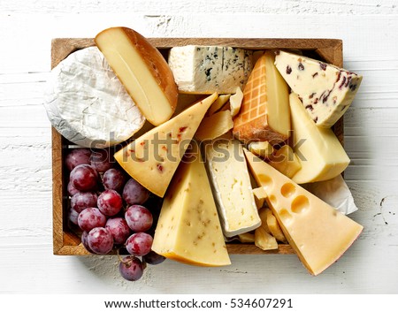 various types of cheese in wooden box on white wooden table, top view