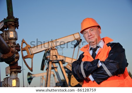 Oil worker in orange uniform and helmet on of background the pump jack and blue sky.