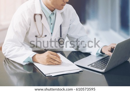 Doctor working with laptop computer and writing on paperwork in the hospital.