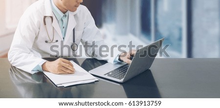 Doctor working with laptop computer and writing on paperwork. Hospital background.