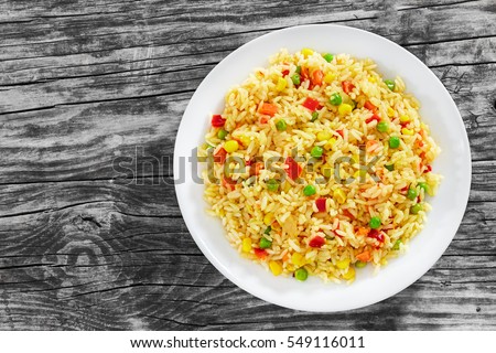 Sweet Corn, red bell pepper, green peas delicious healthy Risotto on white plate on old wooden table, view from above