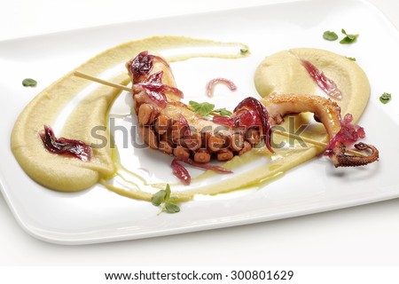 gourmet fish dish, braised octopus on chickpea cream with caramelized onions on white square plate