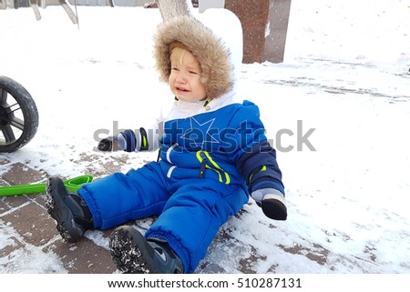 Cute toddler boy fell on winter park road with snow