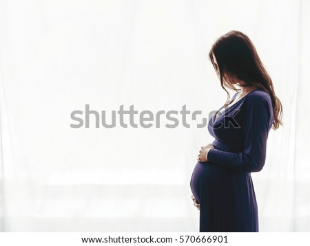 Pregnant woman standing against the window