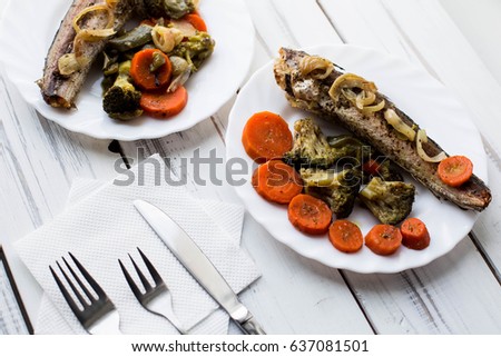 Baked roasted fried fish with baked, baked, gifted vegetables on a white wooden table
