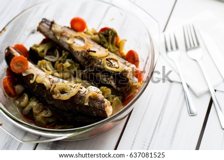 Baked roasted fried fish with baked, baked, gifted vegetables on a white wooden table