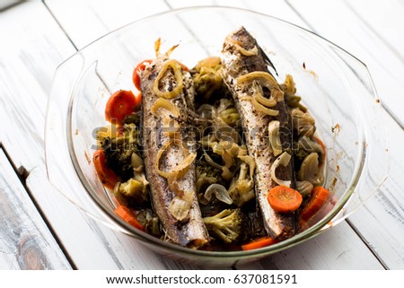 Baked roasted fried fish with baked, baked, gifted vegetables on a white wooden table