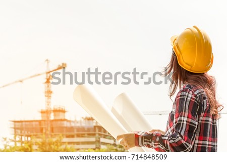 A portrait of engineer woman looking construction. Asian woman architect with blueprint in hand and yellow helmet with select focus and use effect filter. Concept Engineer and business work.