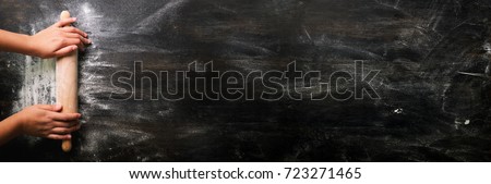 Girl hands keep rolling pin with flour on dark black table, baking background, top view, copy space for your text, meru, recipe. Banner