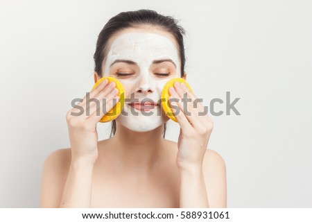 brunette with cream on her face and a sponge in his hands closed eyes.
