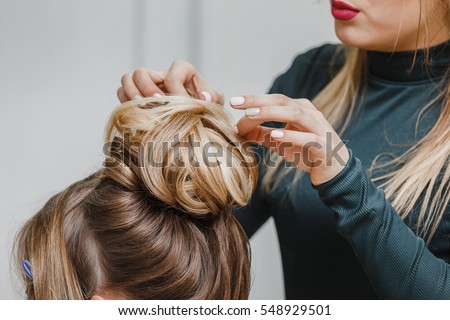 Hairdresser makes upper bun hairstyle close-up on brown hair of beautiful woman