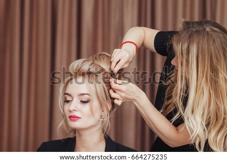 Beautiful blonde girl with long hair doing an professional evening hairdress in a beauty salon