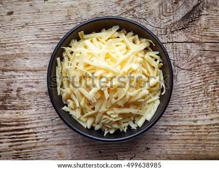 Bowl of grated cheese on wooden background. top view