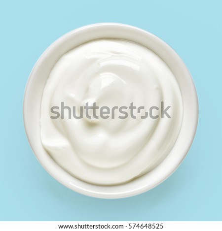 White bowl of cream on light blue background, top view