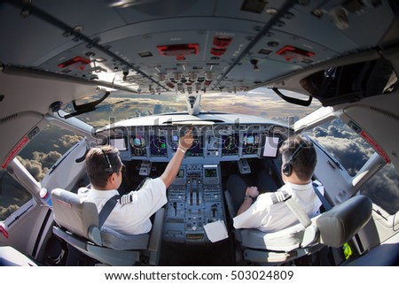 Flight Deck of modern passenger aircraft. Cockpit view in flight during the sunset. Aircraft Pilots at work.