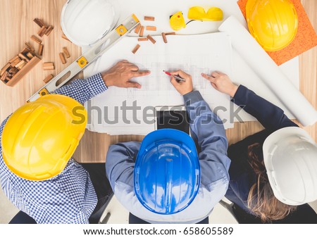 Group of engineers and architects discussing on table with drawing/blueprint, wearing safety helmet working for industrial construction and engineering
