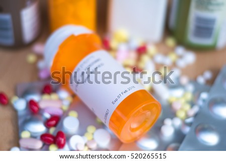 Pile of various expired prescription medicines and bottle focused on expired date. Antibiotic , paracetamol, vitamins drugs on wood background.