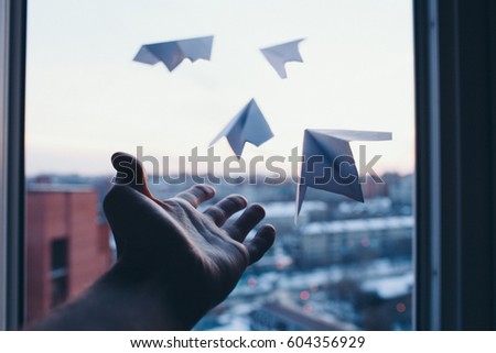 A man's hand lets go little paper planes out of window to nowhere