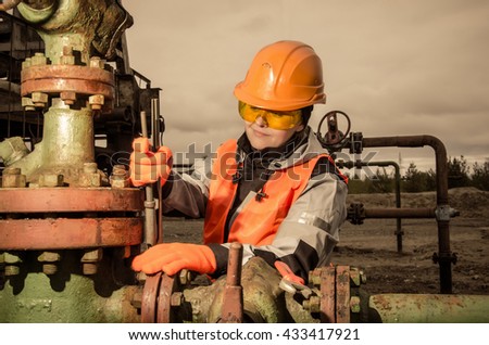 Woman engineer in the oil field repairing wellhead with the wrench wearing orange helmet and work clothes. Oil and gas concept. Toned.
