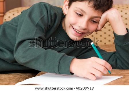 a smiling boy writes a letter on the sofa