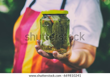 Senior woman holding a jar of pickles in the garden. Homemade pickled cucumbers in a glass jar. Preserving jar of gherkins with mustard seeds and dill.