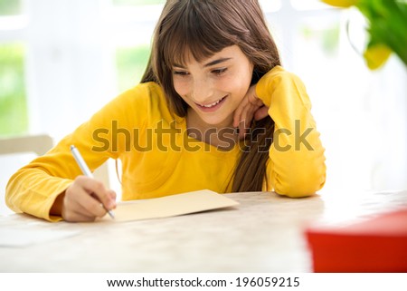 Cute smiling girl writing a letter sitting at desk