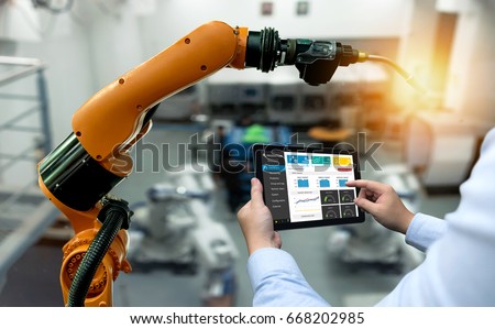 Engineer hand using tablet, heavy automation robot arm machine in smart factory industrial with tablet real time monitoring system application. Industry 4th iot concept.