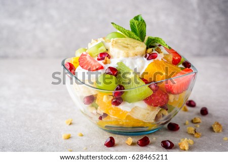 Fresh fruit salad with yogurt and walnuts in glass bowl on stone background. Healthy Eating. Selective focus.