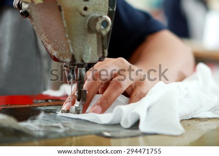 close up portrait of hands of seamstress sewing using industrial sewing machine