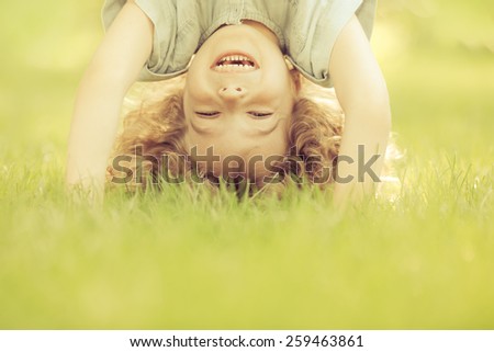Happy child standing upside down on green grass. Laughing kid having fun in spring park. Healthy lifestyle concept