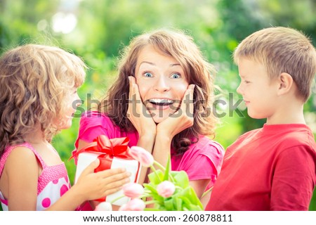 Happy family with bouquet of flowers and gifts outdoors. Young beautiful mother with son and daughter lying on green grass. Spring holiday concept. Mother's day. Surprise and joy