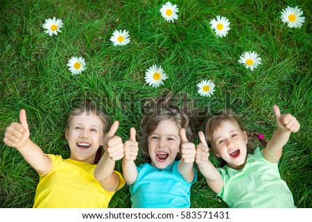 Group of happy children playing outdoors. Kids having fun in spring park. Friends lying on green grass. Top view portrait