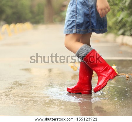 Child wearing red rain boots jumping into a puddle. Close up