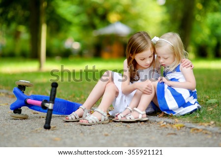 Little girl comforting her sister after she fell while riding her scooter at summer park