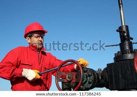 Oil Rig Valve Technician at Work. Oil and Gas Industry.
Oil worker wearing red coveralls and red helmet, working at pump jack oil well.