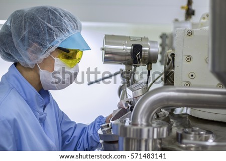 Pharmaceutical Factory Worker in Sterile Environment. Pharmaceutical technician works in sterile working conditions at pharmaceutical factory. Female scientist wearing protective clothing.
