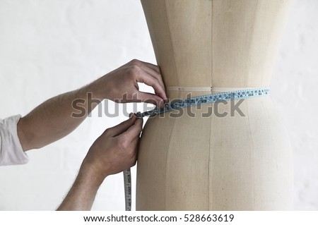 Cropped image of young male tailor measuring mannequin's waist in fashion studio