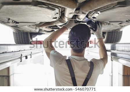 Rear view of automobile mechanic examining car in workshop