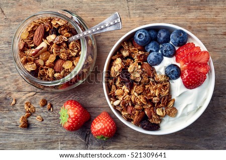 Bowl of homemade granola with yogurt and fresh berries on wooden background from top view