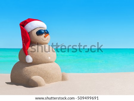 Happy sandy snowman in Christmas Santa Claus hat and sunglasses at sunny sea beach, New Year holiday vacation concept for traveling to hot south countries