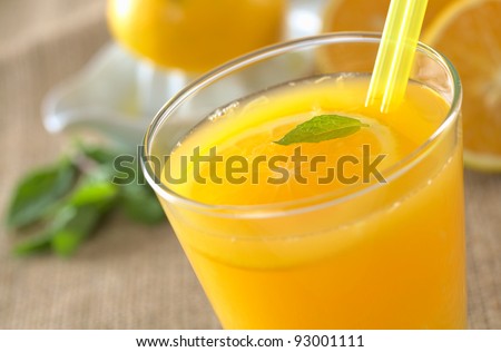 Freshly squeezed orange juice with drinking straws and orange slice, mint leaf on top of the juice (Selective Focus, Focus on the mint leaf in the glass)