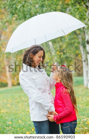 Cute girl with her mother with white umbrella walking in the autumn park. Rain, yellow leaves, tree.